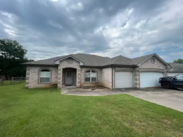 A light-brick ranch with a grey roof and a double garage under a cloudy sky