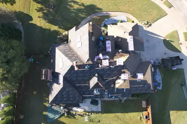 Overhead drone view of a large roof mid-replacement with crew and staged shingle bundles across the deck