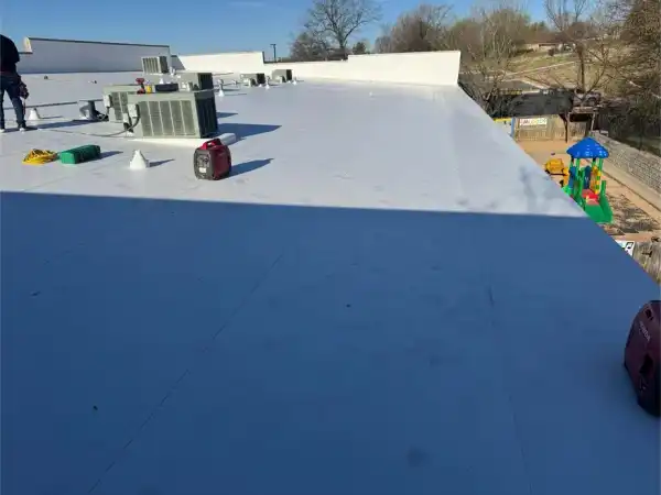The edge of a TPO roof with rooftop units and a playground beyond
