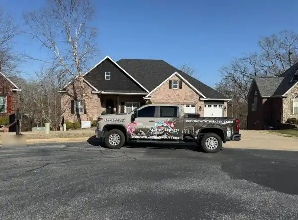 The Roofing & Gutter Experts wrapped pickup parked in front of a brick home with a new charcoal shingle roof