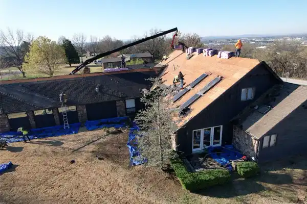 Drone view of a crew working on a long roof with a material lift and blue tarps around the base
