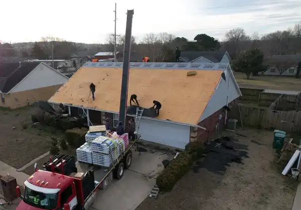 Drone view of a crew on bare roof decking loading shingles from a red boom truck