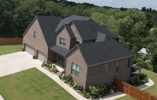 Drone view of a two-storey brick home with a new charcoal roof and flower beds
