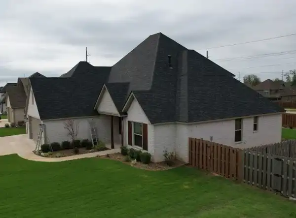 White-brick home with a new charcoal roof, ladders still up, and a cedar fence along the yard