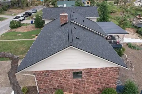Drone view of a brick-and-siding home with a new charcoal roof and thinned trees around it